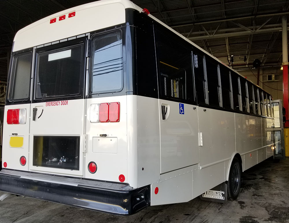 Back right side view of large white bus in garage
